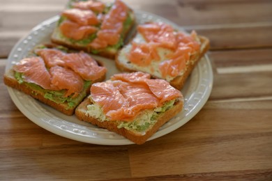 Photo of Sandwiches with avocado spread and salmon on wooden table, closeup