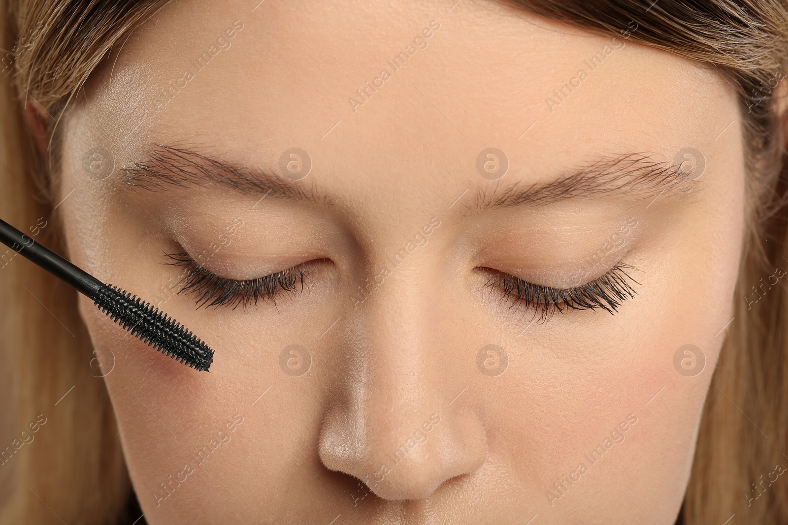 Photo of Woman applying mascara onto eyelashes, closeup view