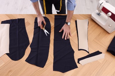 Professional tailor with scissors at table in workshop, above view