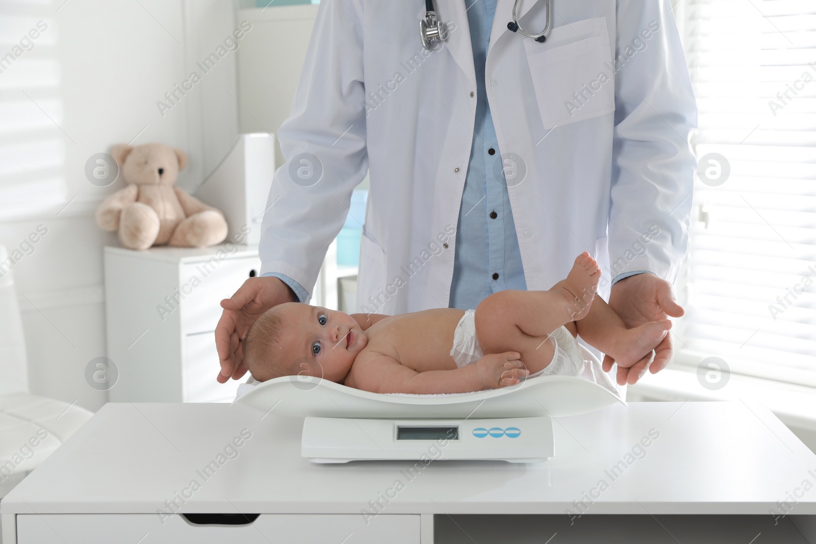 Photo of Pediatrician weighting cute baby in clinic, closeup. Health care