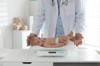 Photo of Pediatrician weighting cute baby in clinic, closeup. Health care