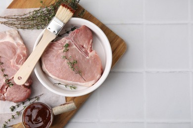 Photo of Raw meat, thyme, basting brush and marinade on white tiled table, top view. Space for text