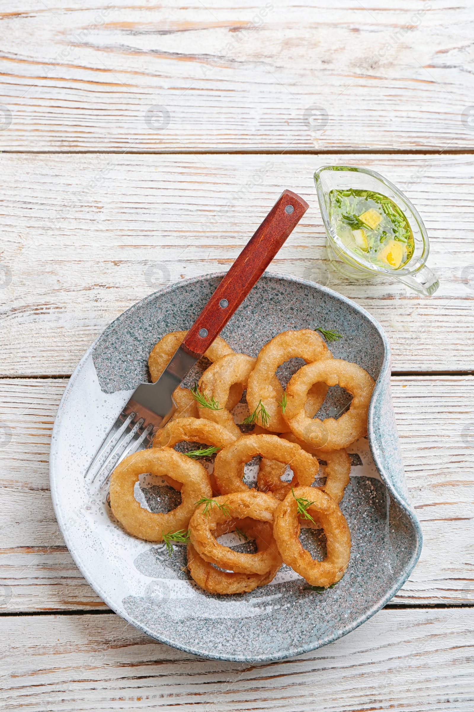 Photo of Fried onion rings served with sauce on wooden background, top view