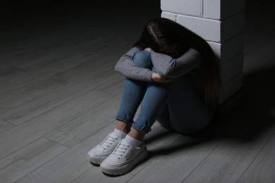Photo of Upset teenage girl sitting at column indoors. Space for text