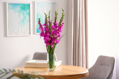 Photo of Vase with beautiful pink gladiolus flowers on wooden table in room, space for text