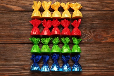 Photo of Many candies in colorful wrappers on wooden table, flat lay