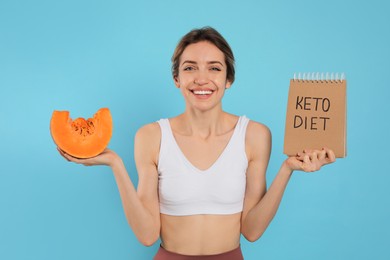 Photo of Woman holding notebook with phrase Keto Diet and pumpkin on light blue background
