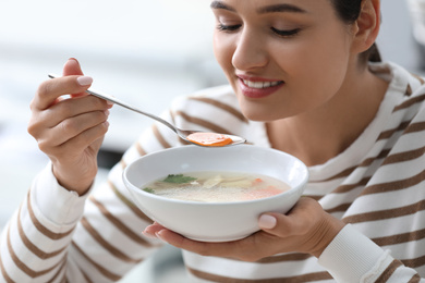 Photo of Young woman eating tasty vegetable soup indoors