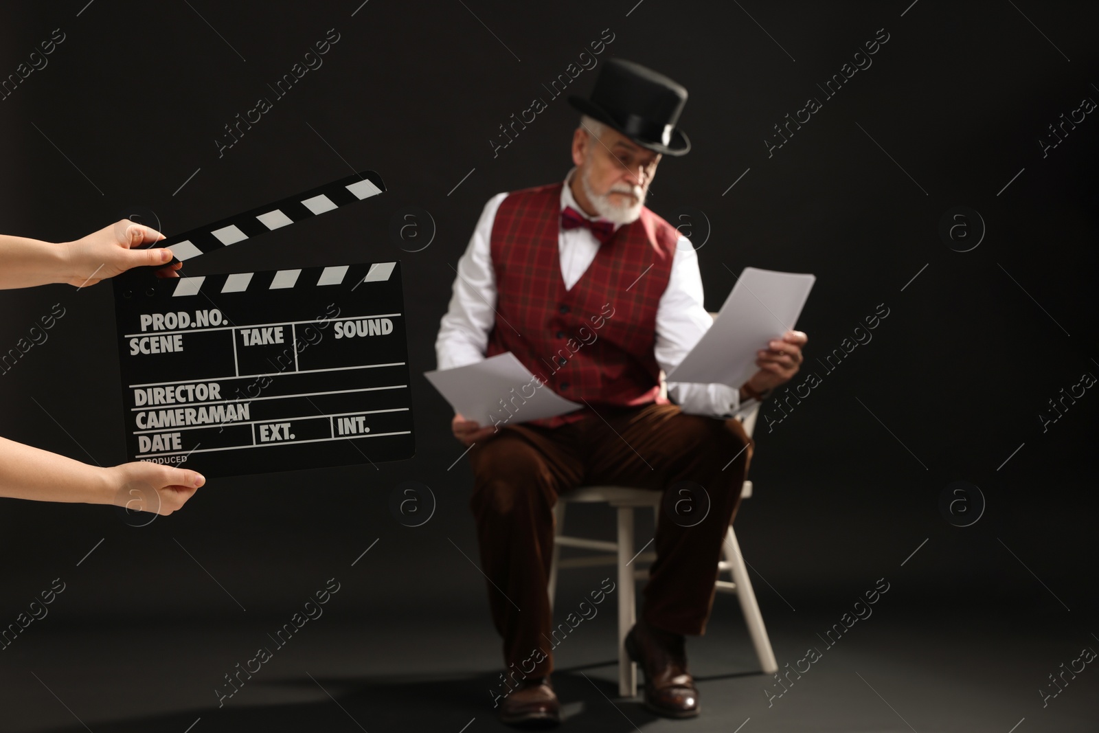 Photo of Senior actor performing role while second assistant camera holding clapperboard on black background, selective focus. Film industry