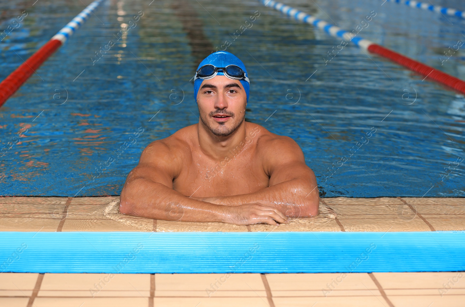 Photo of Young athletic man wearing cap and goggles in swimming pool