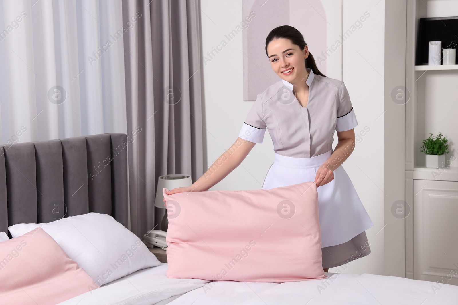 Photo of Young maid making bed in hotel room