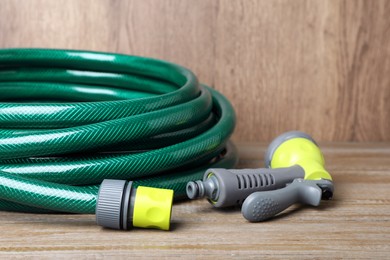 Photo of Green garden hose with spray gun on wooden table