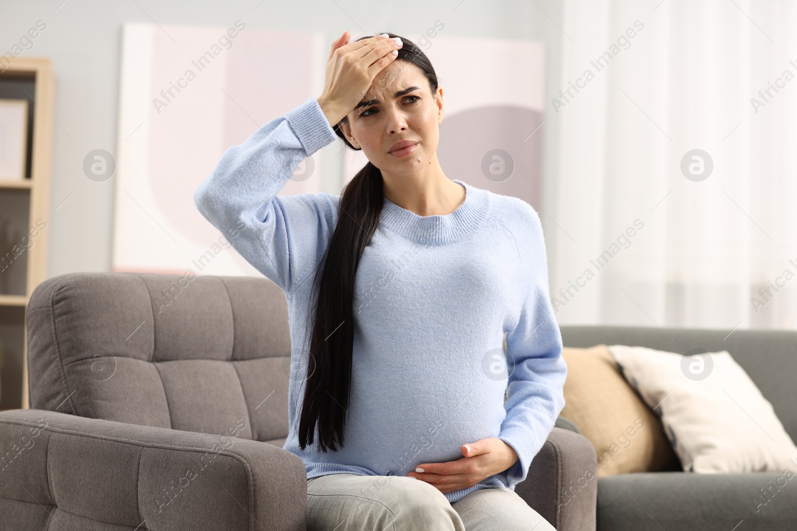 Photo of Pregnant woman suffering from headache on armchair at home