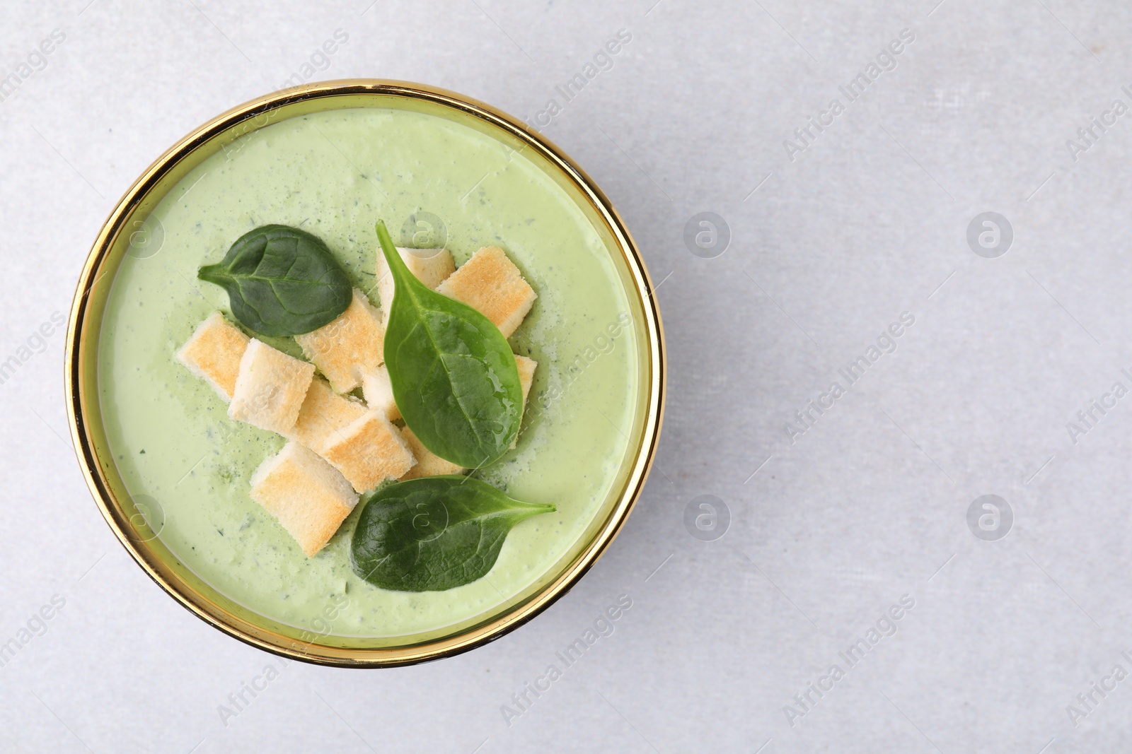 Photo of Delicious spinach cream soup with croutons in bowl on light grey table, top view. Space for text