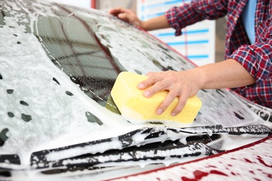 Young man cleaning vehicle with sponge at self-service car wash