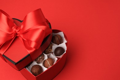 Photo of Heart shaped box with delicious chocolate candies on red table. Space for text