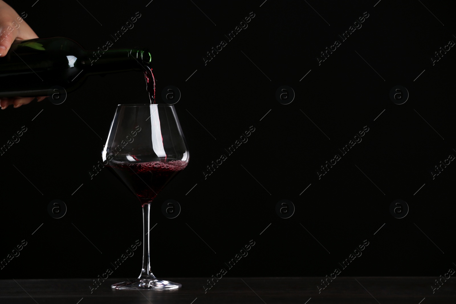 Photo of Woman pouring wine into glass on table against black background, closeup with space for text