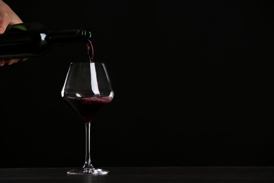 Woman pouring wine into glass on table against black background, closeup with space for text