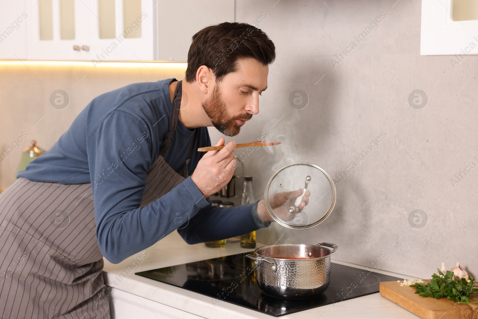 Photo of Man tasting delicious tomato soup in kitchen