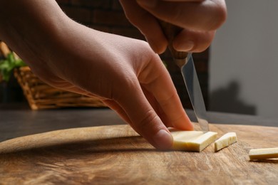 Photo of Woman cutting delicious fresh ripe parsnip at wooden board, closeup