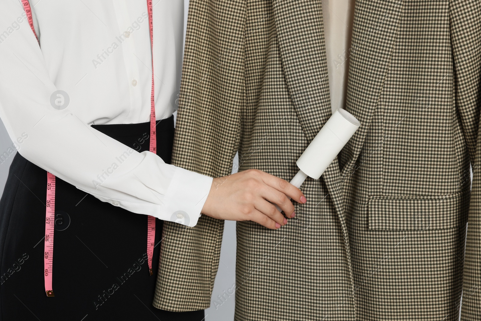 Photo of Woman using adhesive lint roller on light grey background, closeup. Dry-cleaning service