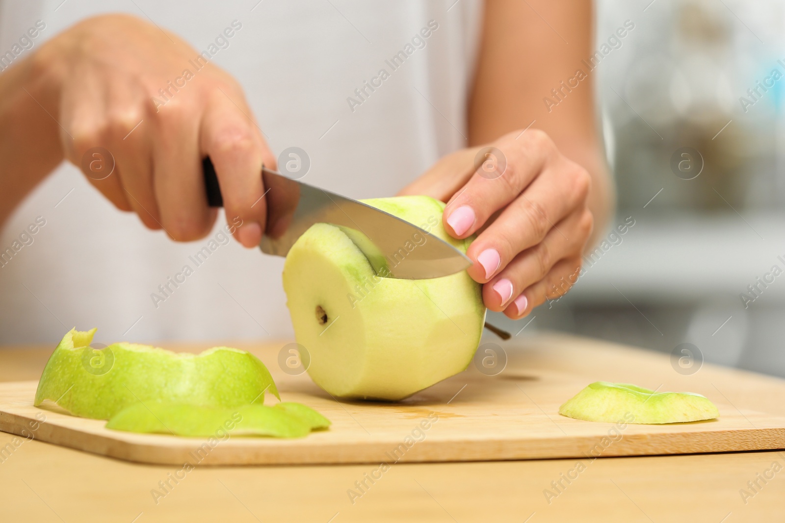 Photo of Woman cutting fresh apple at wooden table indoors, closeup