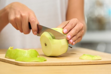 Woman cutting fresh apple at wooden table indoors, closeup