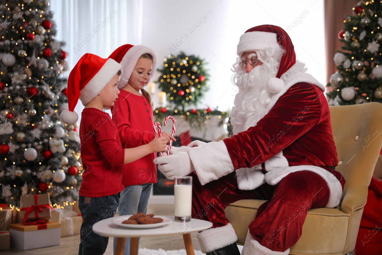 Photo of Santa Claus giving candy canes to children in room decorated for Christmas