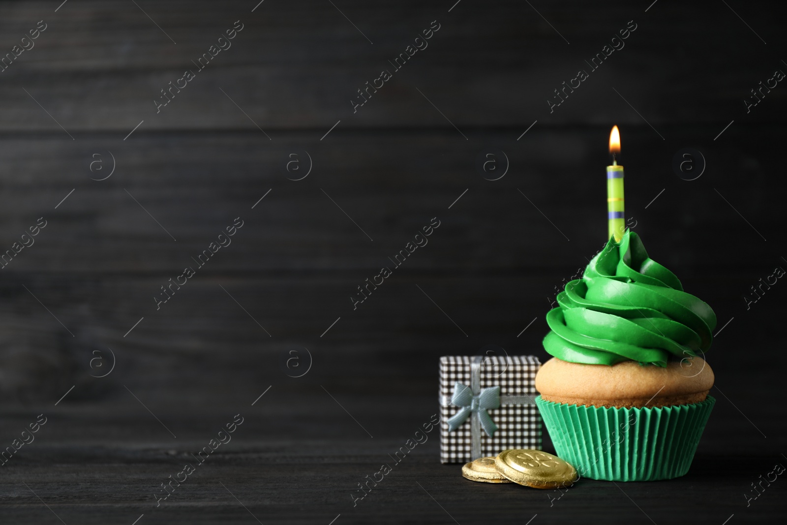 Photo of Decorated cupcake and gift box on black wooden table, space for text. St. Patrick's Day celebration