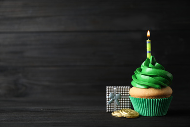 Decorated cupcake and gift box on black wooden table, space for text. St. Patrick's Day celebration