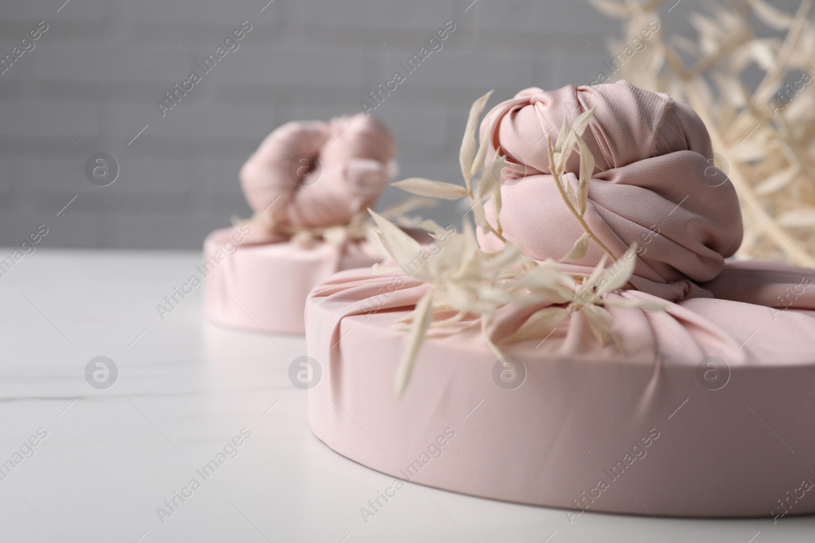 Photo of Furoshiki technique. Gifts packed in pink fabric and dried branches on white table, closeup. Space for text