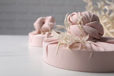 Furoshiki technique. Gifts packed in pink fabric and dried branches on white table, closeup. Space for text