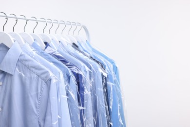 Photo of Dry-cleaning service. Many different clothes in plastic bags hanging on rack against white background, space for text