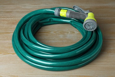 Photo of Green rubber watering hose with nozzle on wooden surface