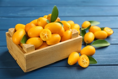 Photo of Fresh ripe kumquats in crate on blue wooden table
