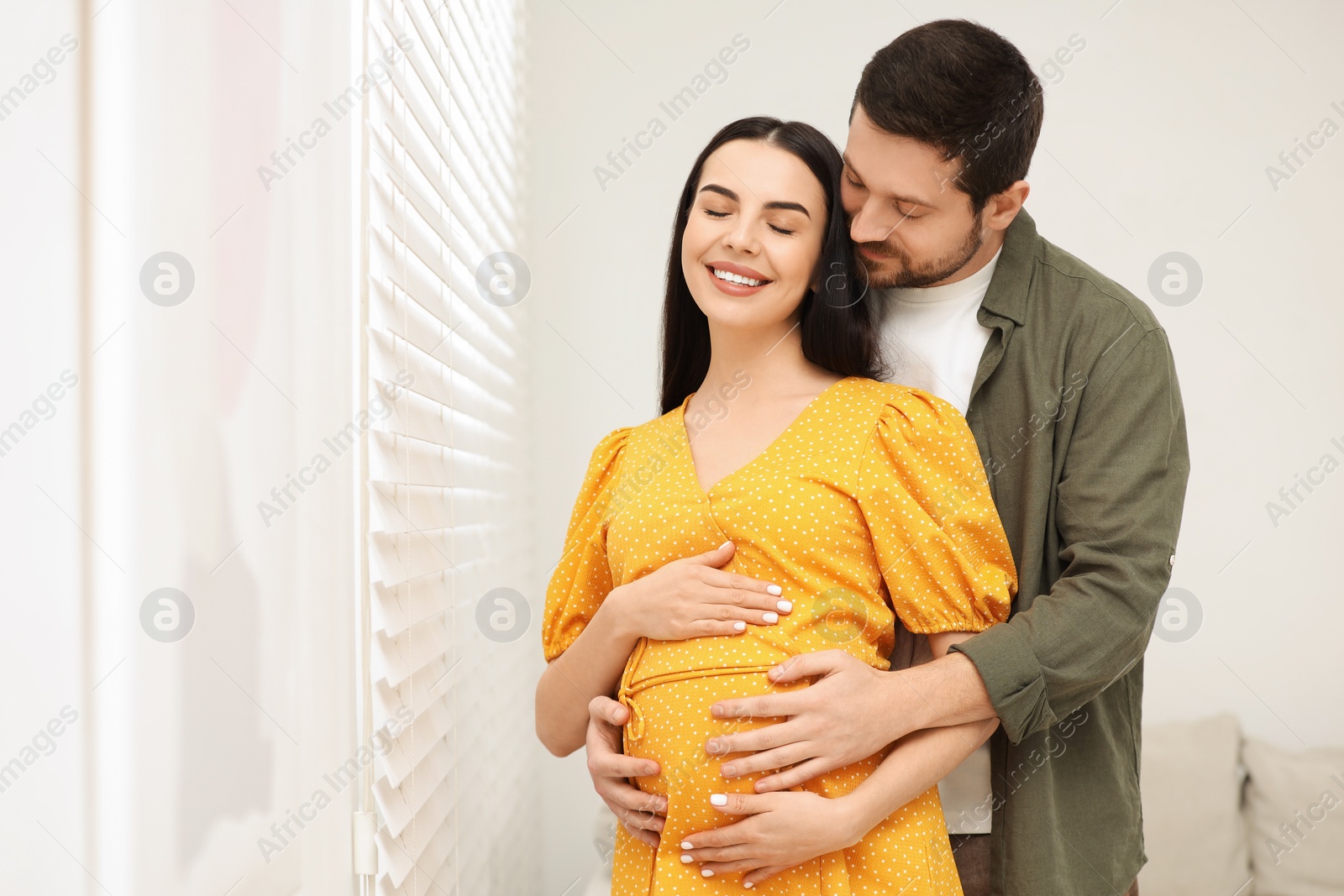 Photo of Happy pregnant woman with her husband indoors, space for text