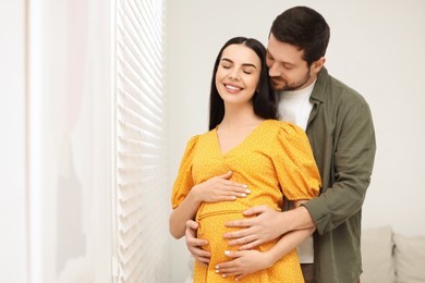 Photo of Happy pregnant woman with her husband indoors, space for text