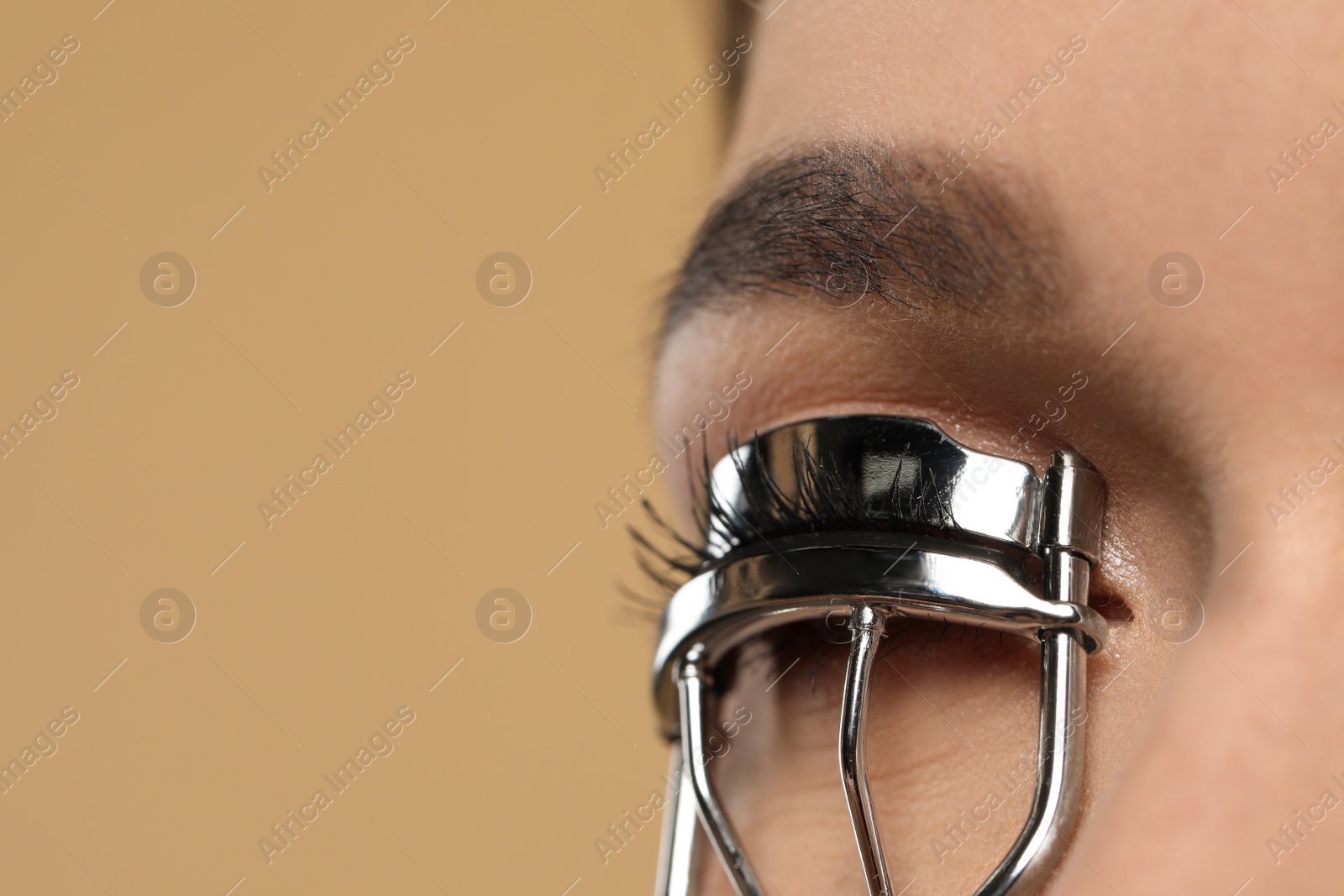 Photo of Woman using eyelash curler on beige background, closeup. Space for text