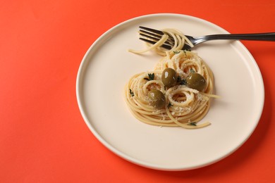 Photo of Heart made of tasty spaghetti, fork, olives and cheese on coral background. Space for text