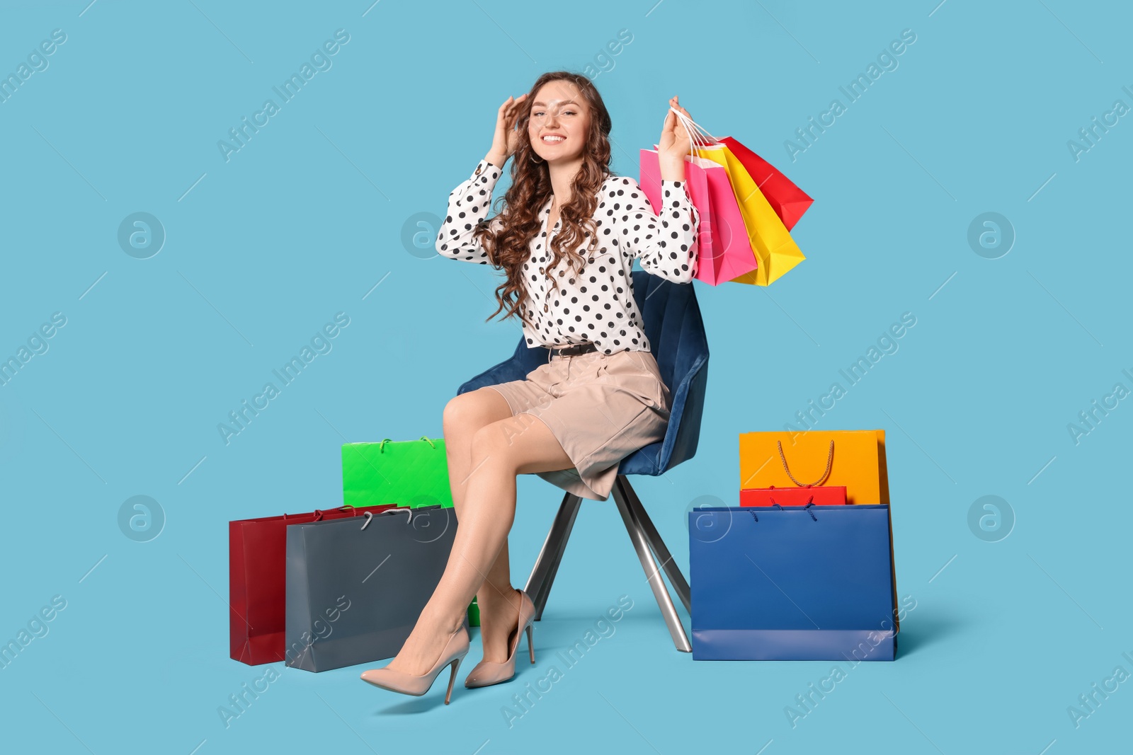 Photo of Happy woman holding colorful shopping bags on armchair against light blue background