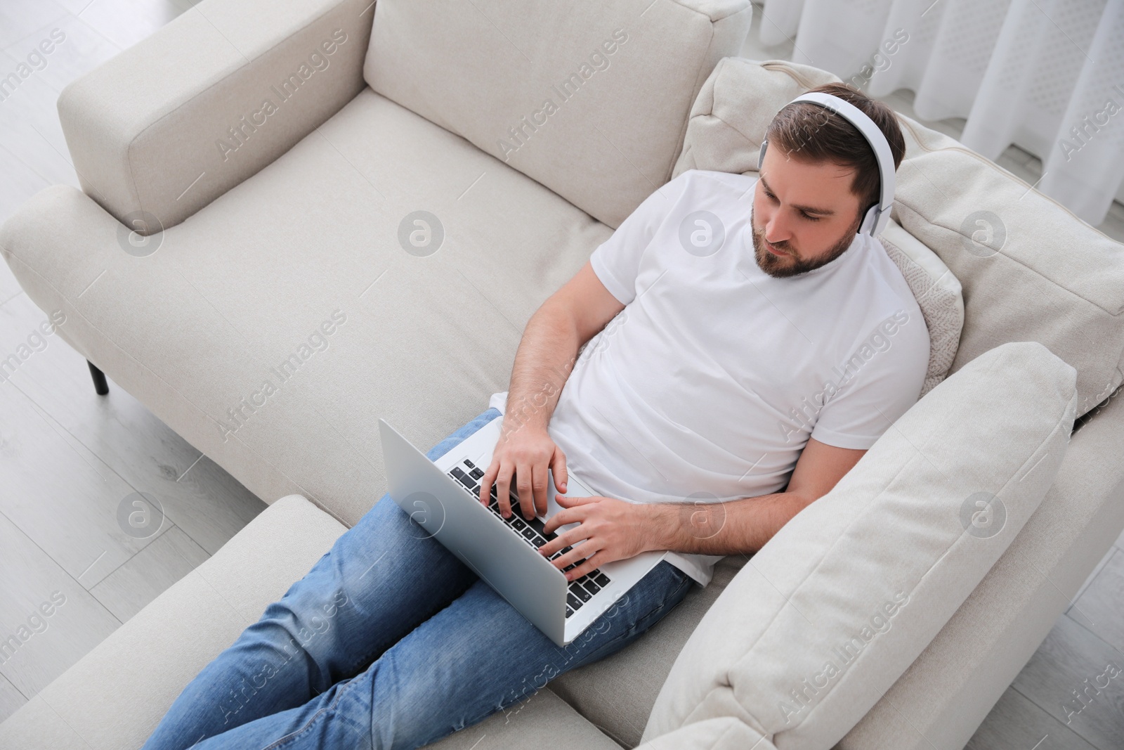 Photo of Man with laptop and headphones sitting on sofa at home