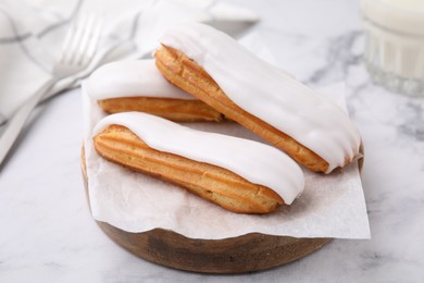 Photo of Delicious eclairs covered with glaze on white marble table, closeup