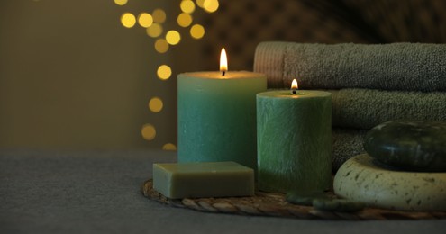 Photo of Spa composition. Burning candles, stones, soap and towels on grey table, space for text