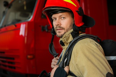 Portrait of firefighter in uniform near red fire truck at station