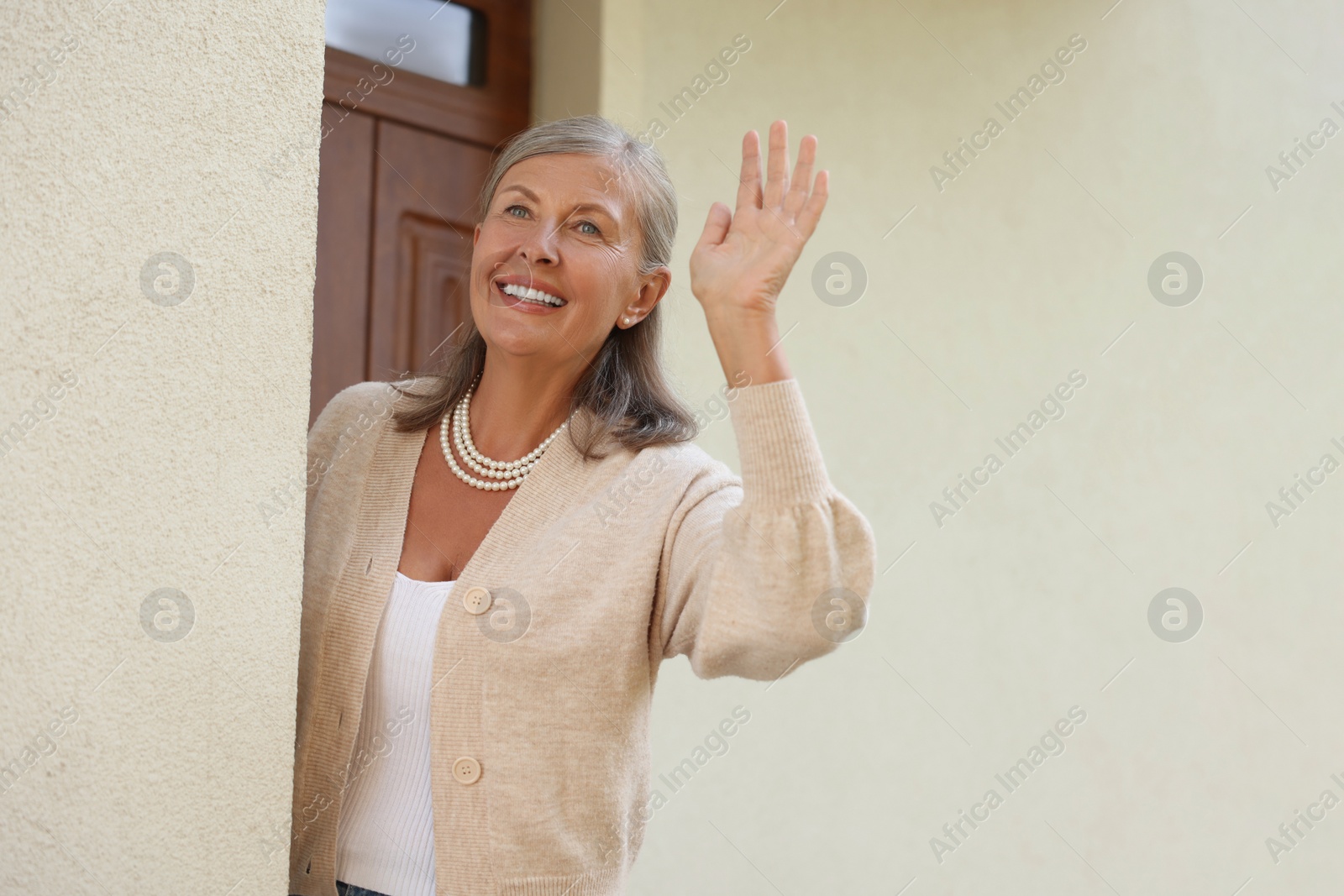 Photo of Neighbor greeting. Happy senior woman waving near house outdoors, space for text