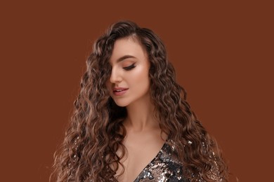 Photo of Beautiful young woman with long curly hair in sequin dress on brown background
