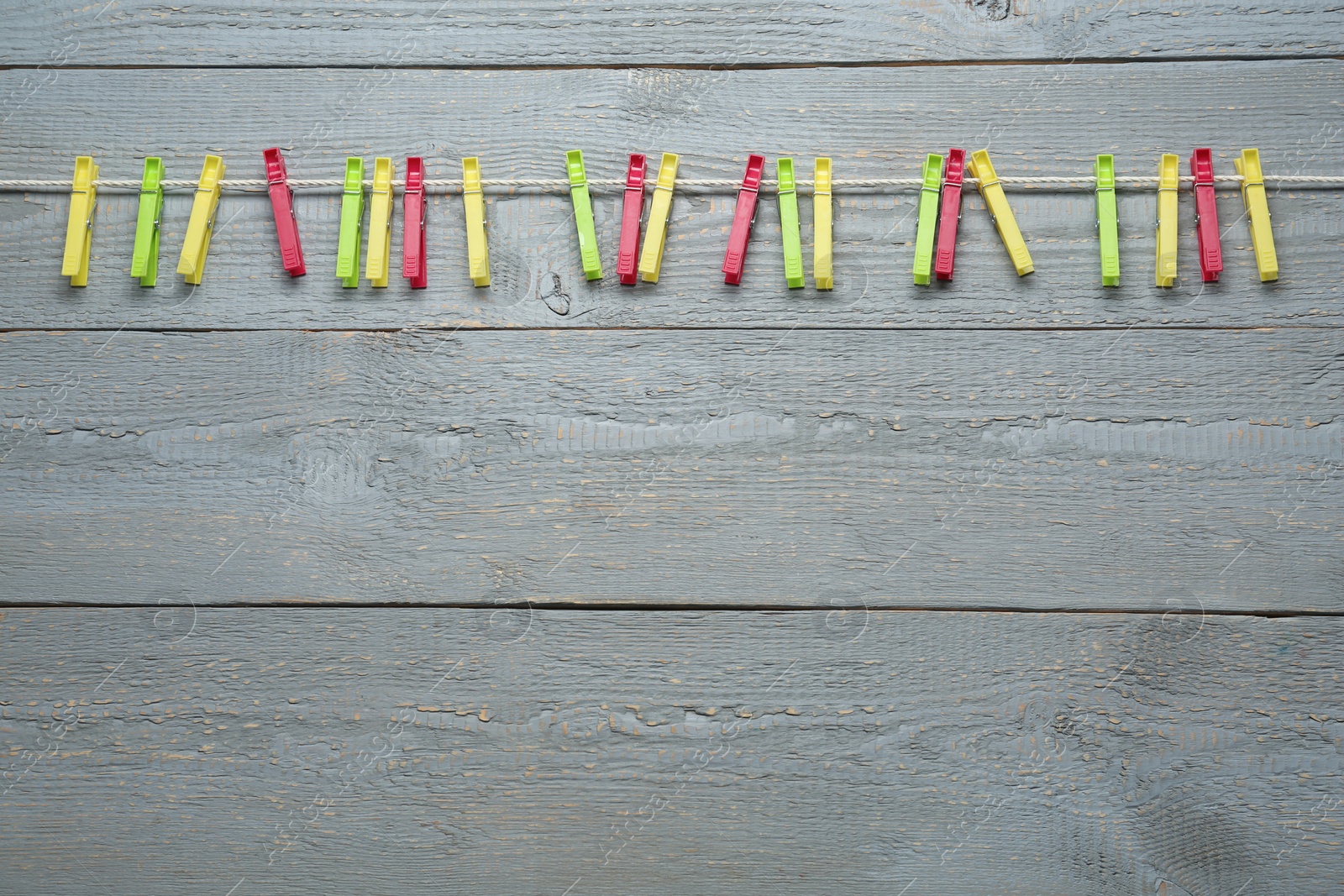 Photo of Colorful plastic clothespins and rope on grey wooden background. Space for text