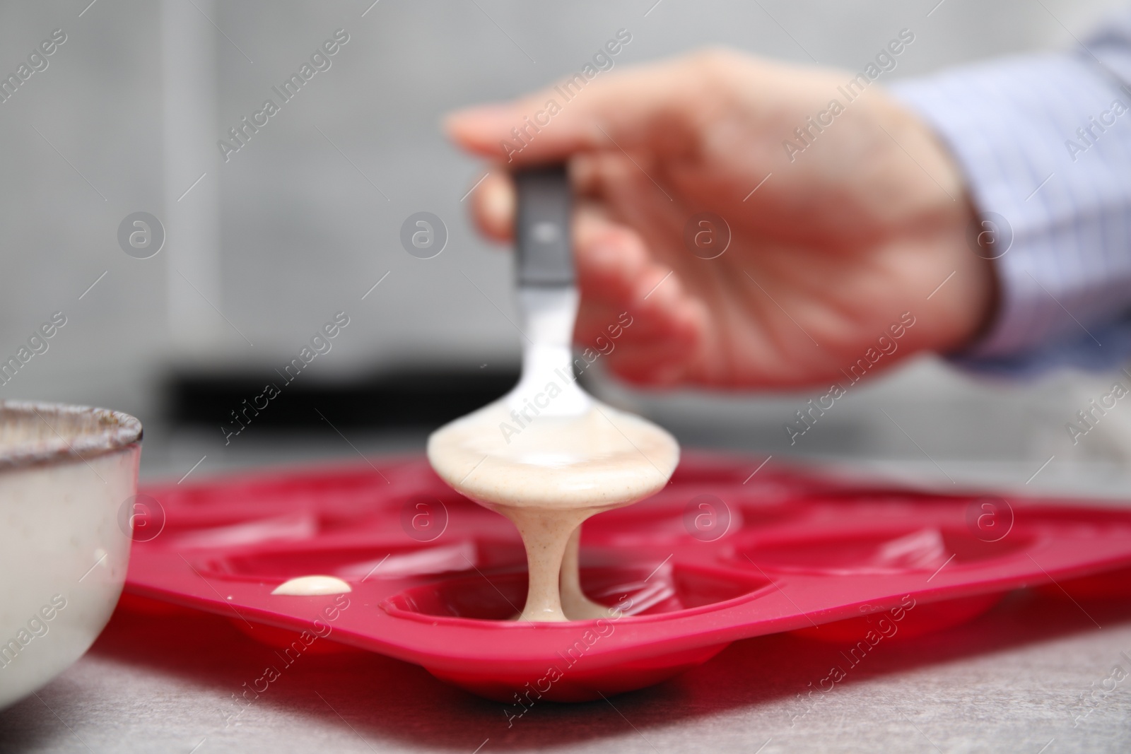 Photo of Woman pouring batter into baking mold at table, closeup. Madeleine cookies