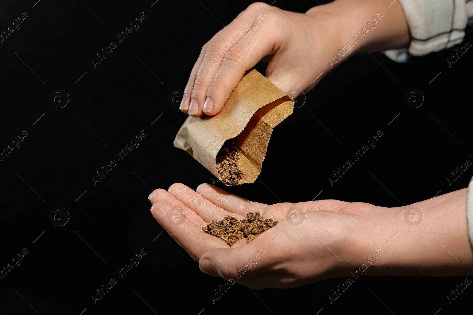 Photo of Woman pouring beet seeds from paper bag into hand on black background, closeup. Vegetable planting