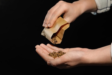 Woman pouring beet seeds from paper bag into hand on black background, closeup. Vegetable planting